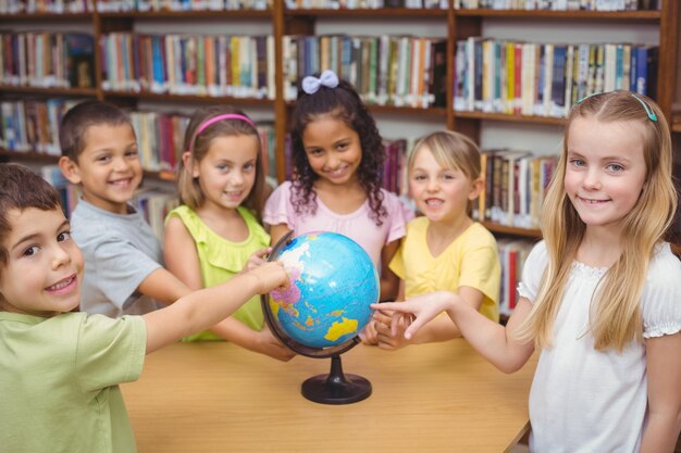 Alunni che sorridono alla macchina fotografica in biblioteca che indica il globo