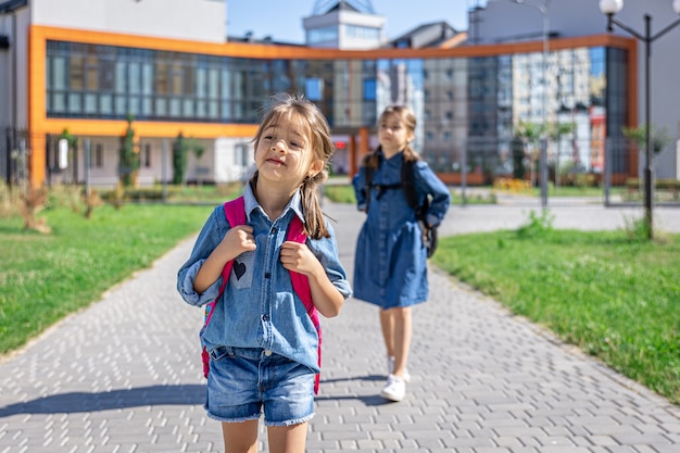 Alunni della scuola primaria. Ragazze con zaini vicino all'edificio all'aperto. Inizio delle lezioni. Primo giorno d'autunno.