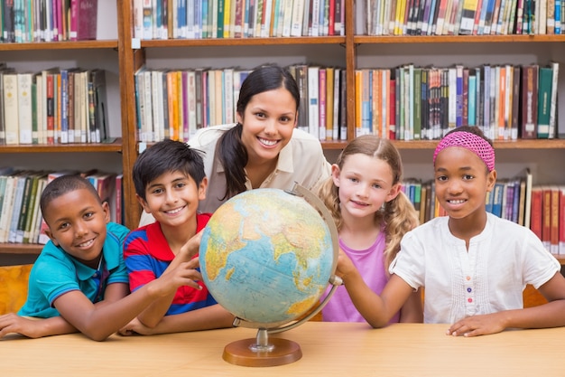 Alunni ed insegnante svegli che esaminano globo in biblioteca