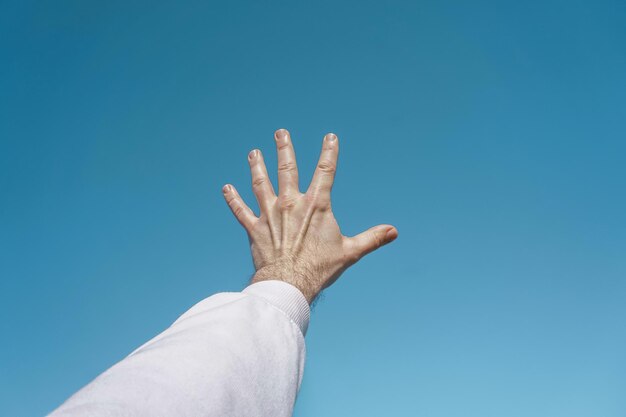 alzare la mano in aria gesticolando nel cielo blu, sfondo blu