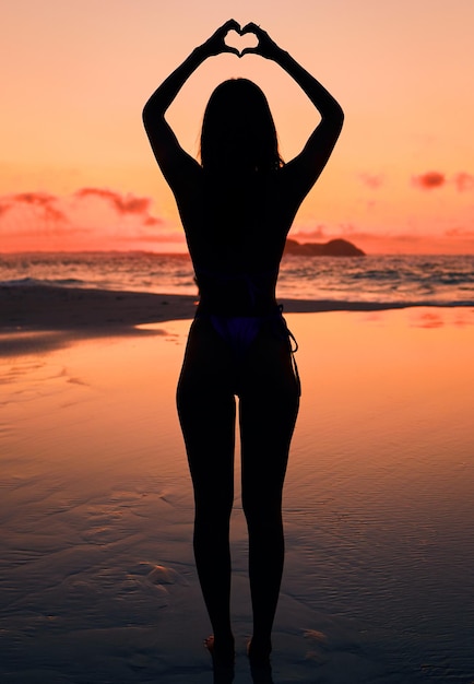 Alzati con il sole. Inquadratura di una donna irriconoscibile che tiene un cuore con le mani sopra la testa in spiaggia.