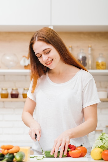 Ama cucinare. Abitudini alimentari sane. Tempo libero e stile di vita. Sorridente giovane donna tagliare le verdure per insalata.