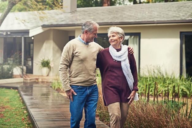 Ama il giardino e la coppia anziana che cammina vicino alla loro casa per il benessere aria fresca e legame Buon pensionamento e uomo e donna anziani su un sentiero insieme nel loro giardino nella loro casa moderna