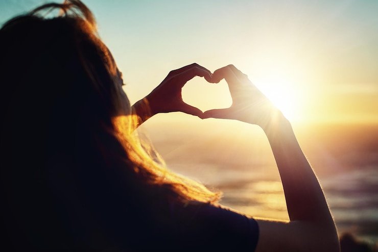 Foto ama il tramonto colpo di retrovisione di una donna che fa una forma di cuore con le mani all'esterno