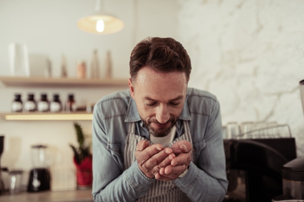 Ama il tuo lavoro. Sorridente proprietario del caffè annusare i chicchi di caffè appena tostati nelle sue mani.