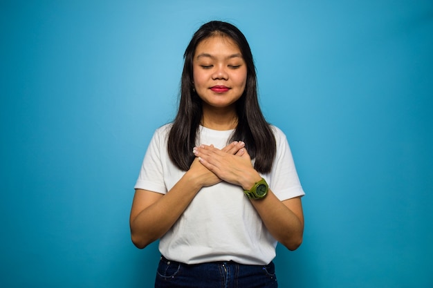 Ama te stesso e grato della bella donna asiatica che indossa una camicia bianca isolata sul blu