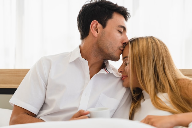 Amante delle coppie che sorride e che fa bacio caldo sulla fronte della donna in camera da letto