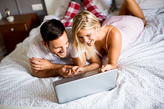 Amanti intimi con laptop sdraiati sul letto in camera da letto