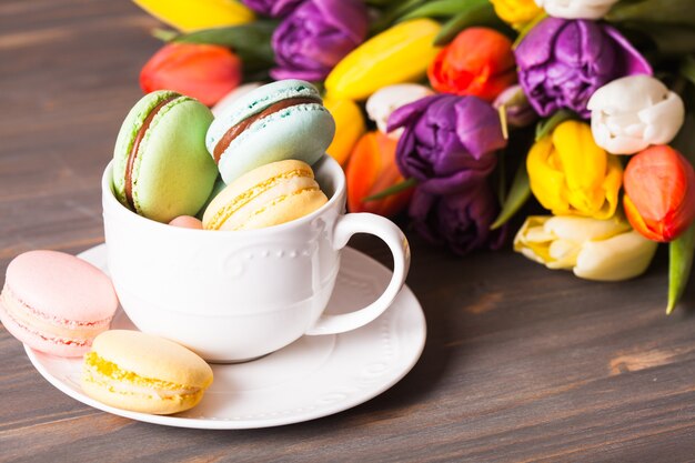 Amaretti colorati in una tazza e fiori sullo sfondo