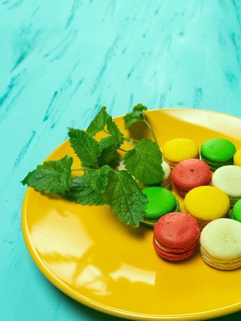 Amaretti colorati sul piatto giallo sulla tavola di legno. Copia spazio.