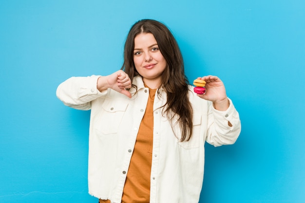 Amaretti curvy della holding della giovane donna che mostrano un gesto di avversione, pollici giù. Concetto di disaccordo.