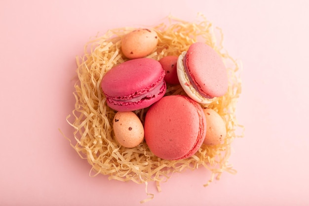 Amaretti magenta e rosa e uova di cioccolato in nido di carta decorativa su sfondo rosa pastello vista dall'alto da vicino