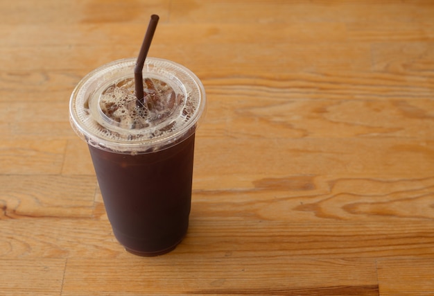 Americano ha ghiacciato il caffè in tazza di plastica asportabile sullo scrittorio di legno nel negozio del caffè