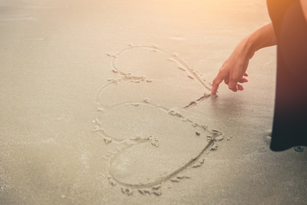 Ami il concetto, cuore di tiraggio della mano delle donne sulla spiaggia.