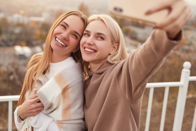 Amiche alla moda felici che prendono selfie sulla terrazza