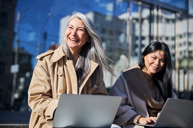 Amiche allegre che usano i laptop per strada