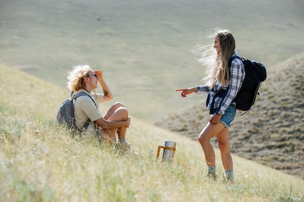 Amiche chiacchierone che fanno un'escursione nelle colline erbose. Riposare sul pendio, parlare, ridere.