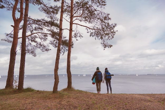 Amiche con zaini che stanno da solo davanti alla vista della foresta e del lago.