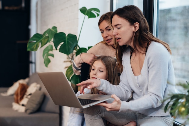 Amiche e una bambina seduta a casa sul davanzale della finestra a guardare un film su un laptop.