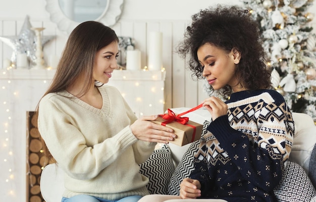 Amiche felici che si scambiano i regali di Natale in un soggiorno decorato