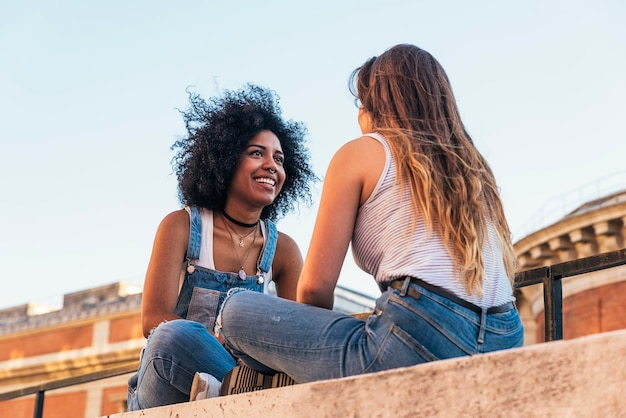 Amiche sedute su un muro di sostegno contro un cielo limpido