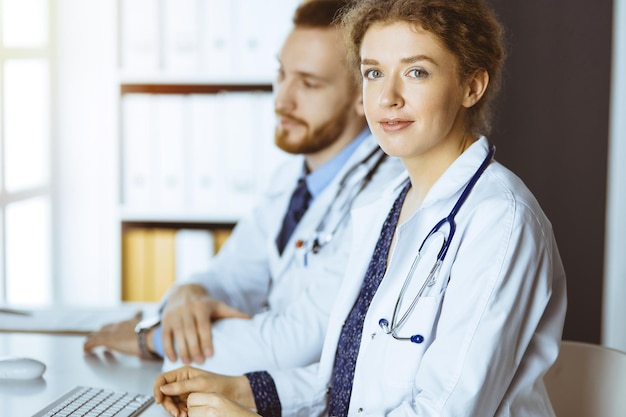 Amichevole dottoressa seduta in clinica con il suo collega maschio sullo sfondo nella clinica soleggiata Concetto di medicina