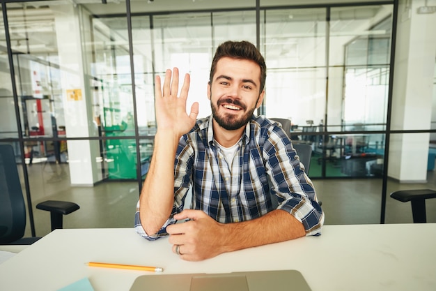 Amichevole ragazzo bruno che agita la mano durante una videochiamata