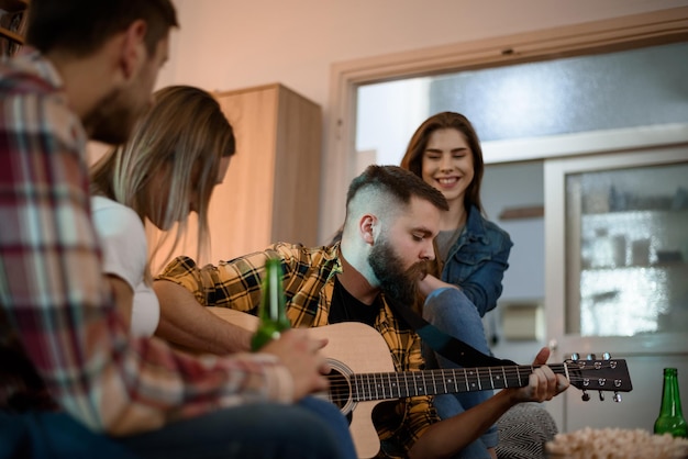 Amici a una festa in casa che suonano la chitarra e bevono birra