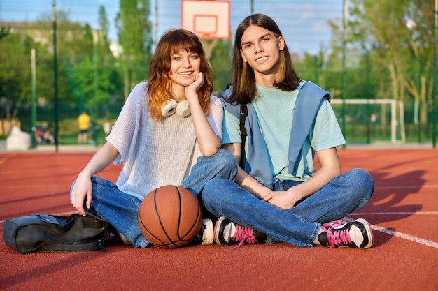 Amici adolescenti ragazzo e ragazza che guarda l'obbiettivo seduto sul campo da basket