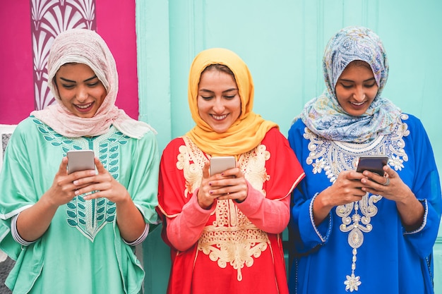 Amici arabi felici utilizzando gli smartphone all'aperto - Giovani ragazze islamiche che si divertono con la nuova tecnologia di tendenza - Influencer e concetto di amicizia - Focus sui volti