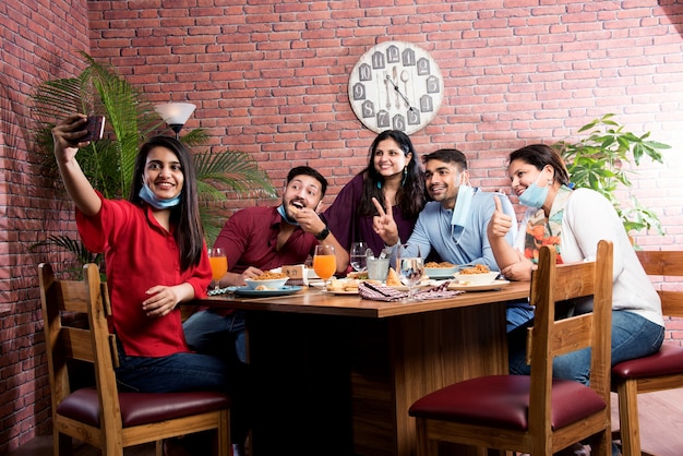 Amici asiatici indiani che mangiano al ristorante Dining Concept indossando una maschera protettiva dopo la pandemia della corona