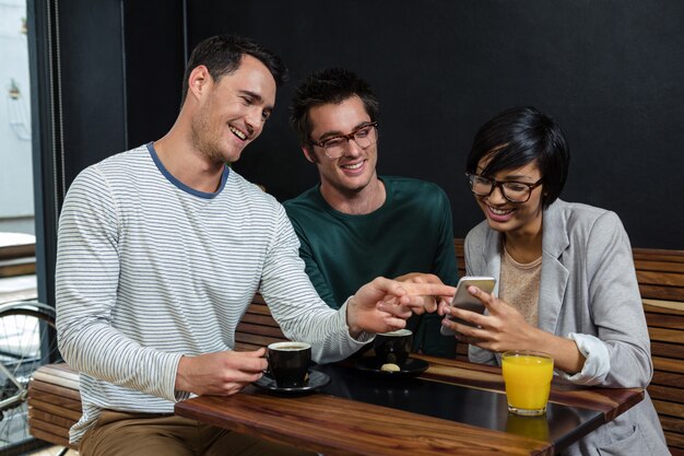 Amici che bevono caffè e succo d'arancia mentre esaminano smartphone