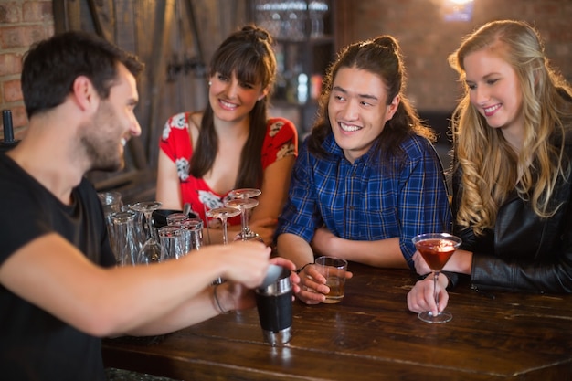 Amici che esaminano il barista che fa le bevande nel pub