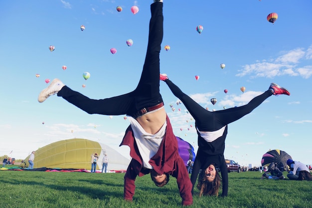 Amici che fanno handstand sul campo erboso contro le mongolfiere in cielo
