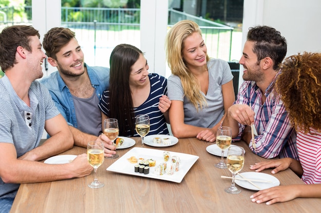 Amici che godono mentre mangiano sushi e vino