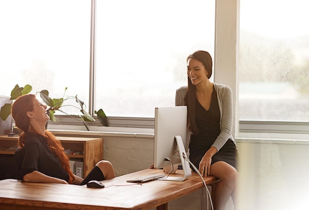 Amici che parlano e donne d'affari in ufficio durante una conversazione chiacchierando e ridendo alla scrivania Collaborazione nella comunicazione e lavoratrici durante una conversazione informale in pausa relax e felici al mattino