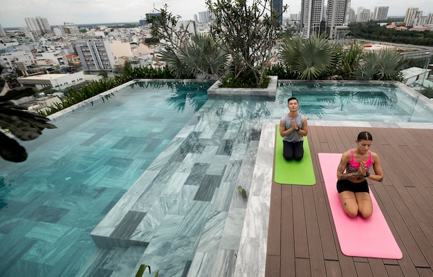 Amici che praticano yoga insieme all'aperto a bordo piscina