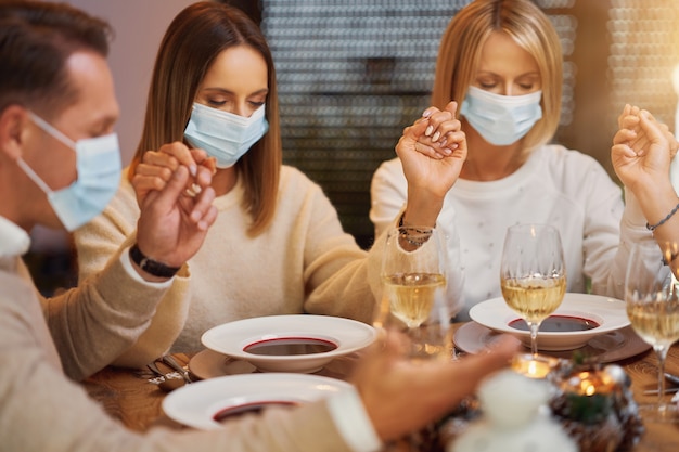 Amici che pregano prima della cena di natale indossando la maschera. Foto di alta qualità