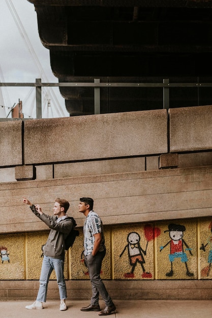 Amici che prendono un selfie da un Amici che prendono selfie da un murale di street art graffiti dell'artista britannico Stik a South Bank, Waterloo, Londra, Regno Unito presi il 22 giugno 2021