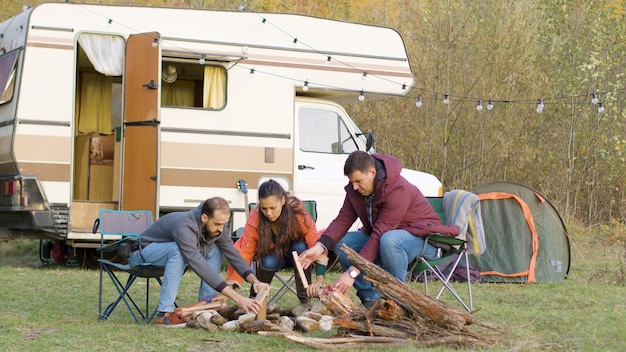 Amici che preparano la legna per il fuoco da campo davanti al camper retrò. Tenda da campeggio.