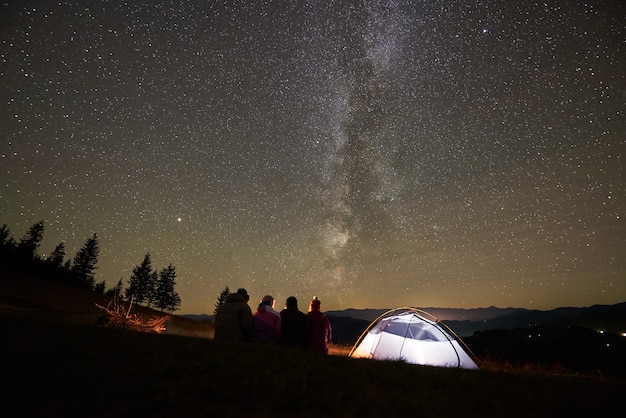 Amici che riposano accanto al campo, falò sotto il cielo stellato notturno