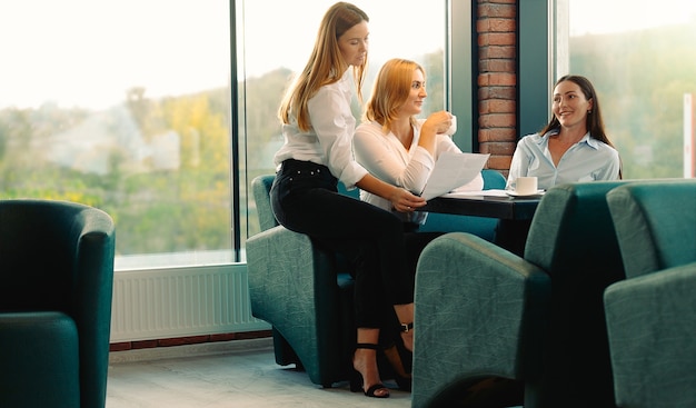 Amici che si divertono a bere il caffè in ufficio moderno il brainstorming nell'ambito di un nuovo progetto. Le giovani donne discutono seduti insieme a tavola trascorrendo del tempo in pausa caffè.