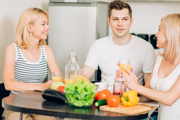 Amici che si rilassano in cucina. Tre studenti caucasici seduti a tavola, pensando a cosa cucinare per cena, bevendo frullati e parlando. Persone, concetto di cibo sano.