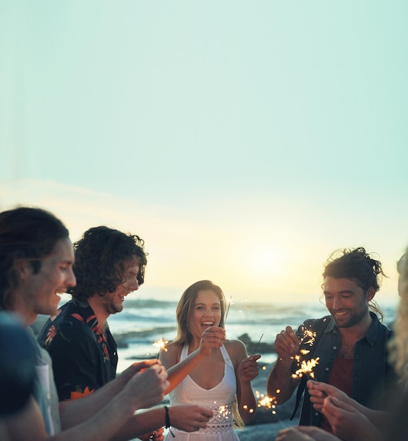 Amici con le stelle filanti che festeggiano il capodanno sulla spiaggia al tramonto