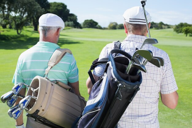 Amici del giocatore di golf che camminano tenendo le loro sacche da golf