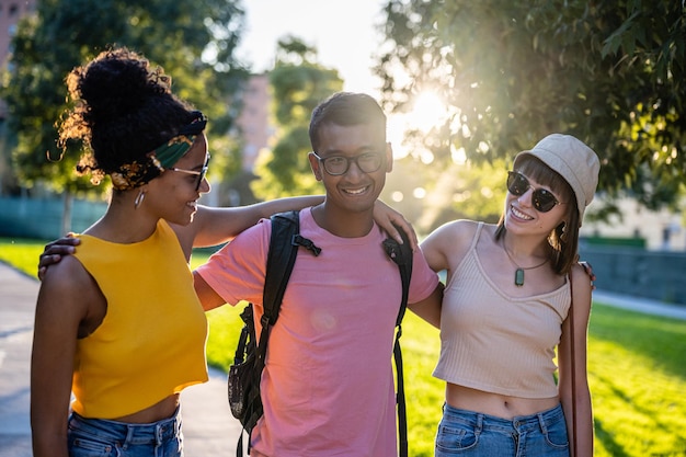 Amici della generazione Z che camminano al tramonto in un parco un ragazzo e due ragazze che si divertono e trascorrono del tempo insieme in vacanza