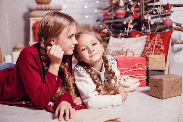 Amici della sorella di ragazze che abbracciano seduto all'albero di Natale, il concetto di infanzia, Natale