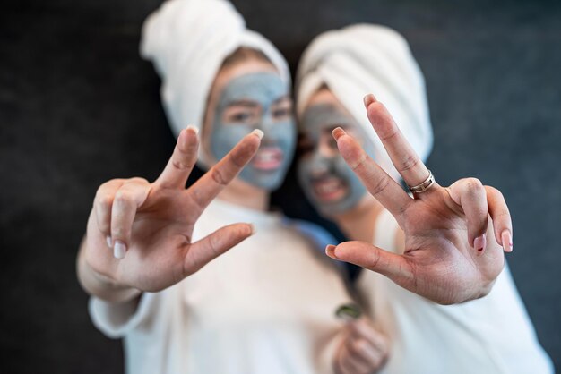 Amici di ragazze in asciugamano bianco che applicano maschera facciale di argilla di fango nero isolata sul nero