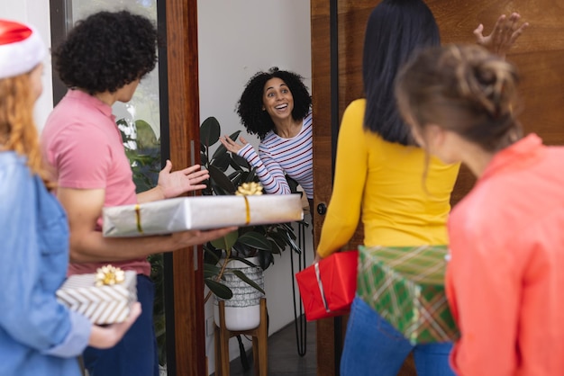 Amici diversi e felici che salutano alla porta con regali a Natale