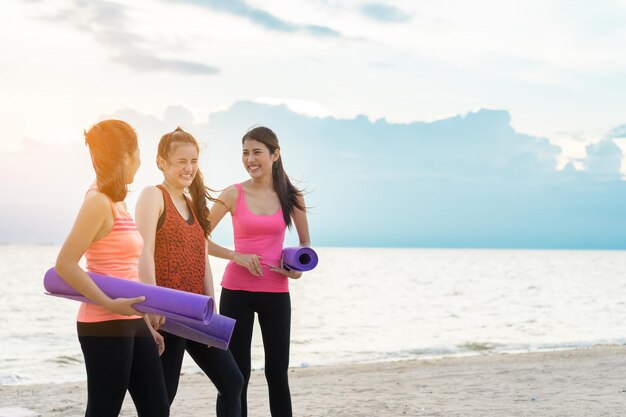 Amici donne che tengono tappetini da ginnastica mentre sono in piedi sulla riva della spiaggia